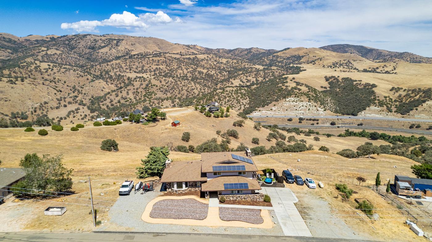 Aerial view of 19904 Dovetail Ct — home with owned solar panels on Golden Hills acreage, Tehachapi mountains behind