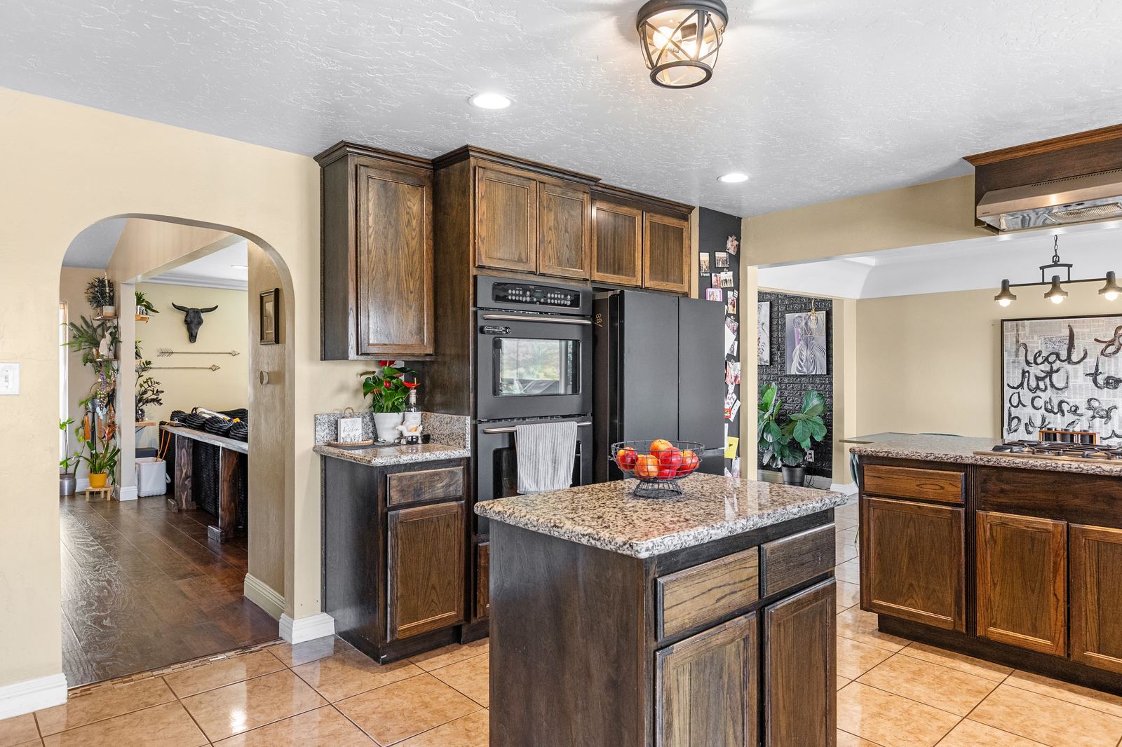 Kitchen island with granite top, double wall ovens and an archway to the adjoining room
