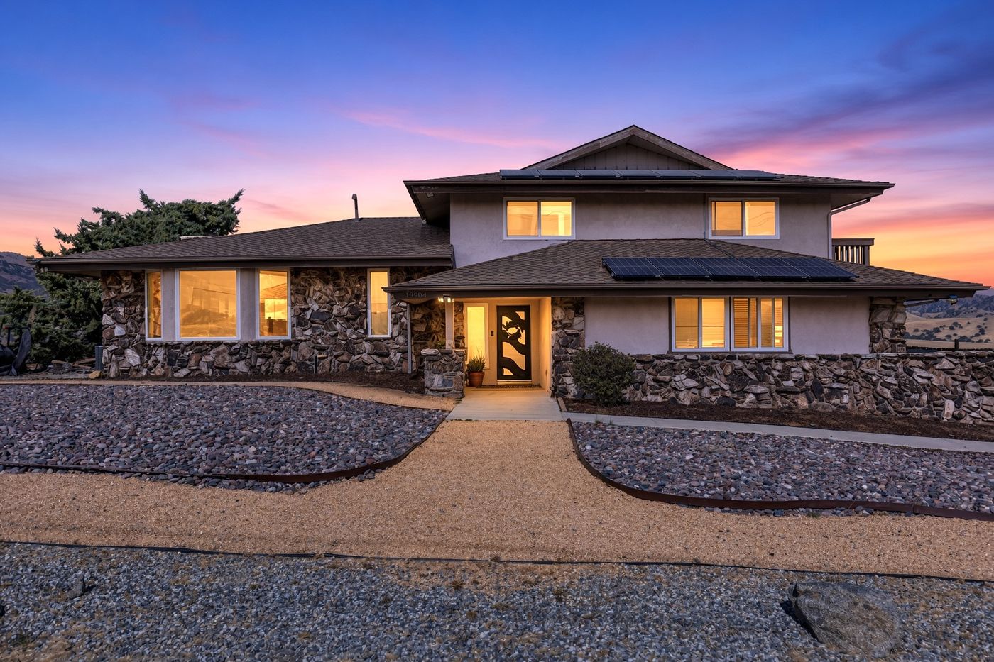 Front exterior of 19904 Dovetail Ct at twilight — stone-and-stucco home with lit windows and owned solar panels