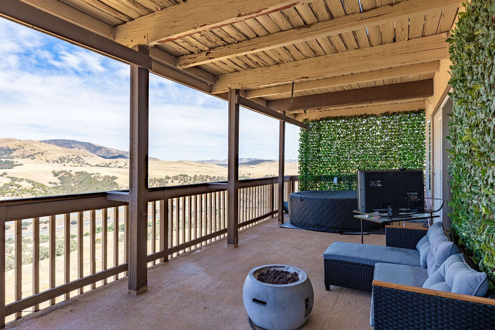 Covered upper deck with hot tub, lounge seating, fire bowl and a panoramic view across the golden hills